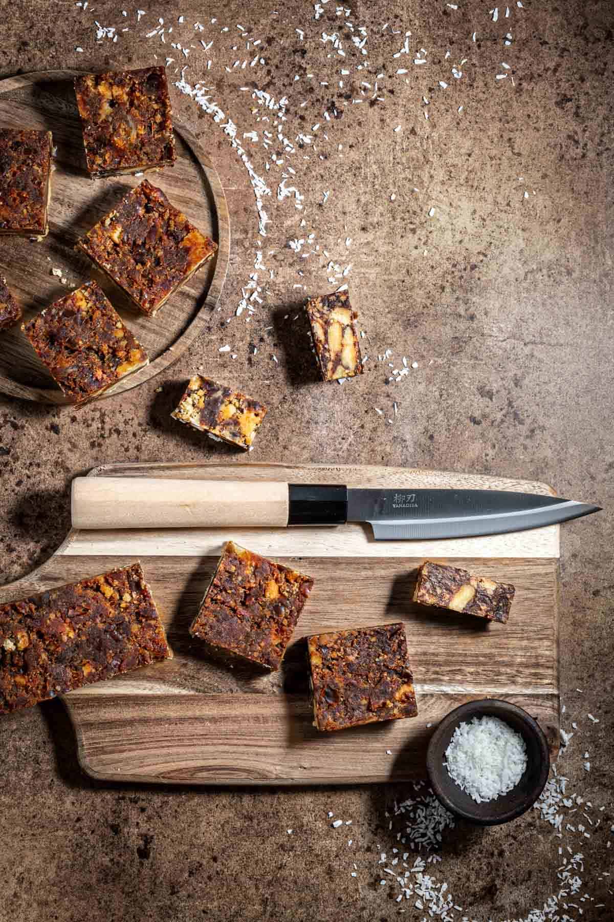 Sliced date squares on a wooden chopping board with a knife.