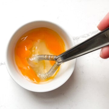 Whisking an egg in a small white bowl.
