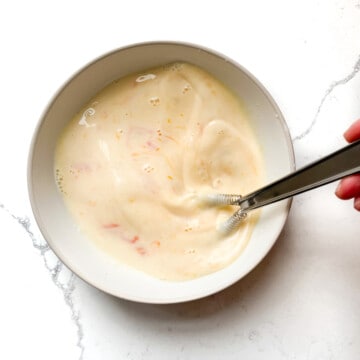 Whisking together milk and eggs in a small white bowl.