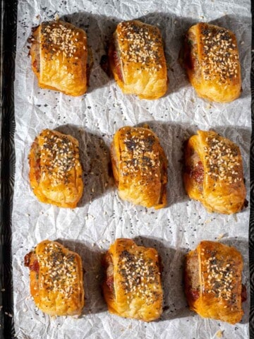 Mini homemade sausage rolls with puff pastry and chorizo on a baking tray.