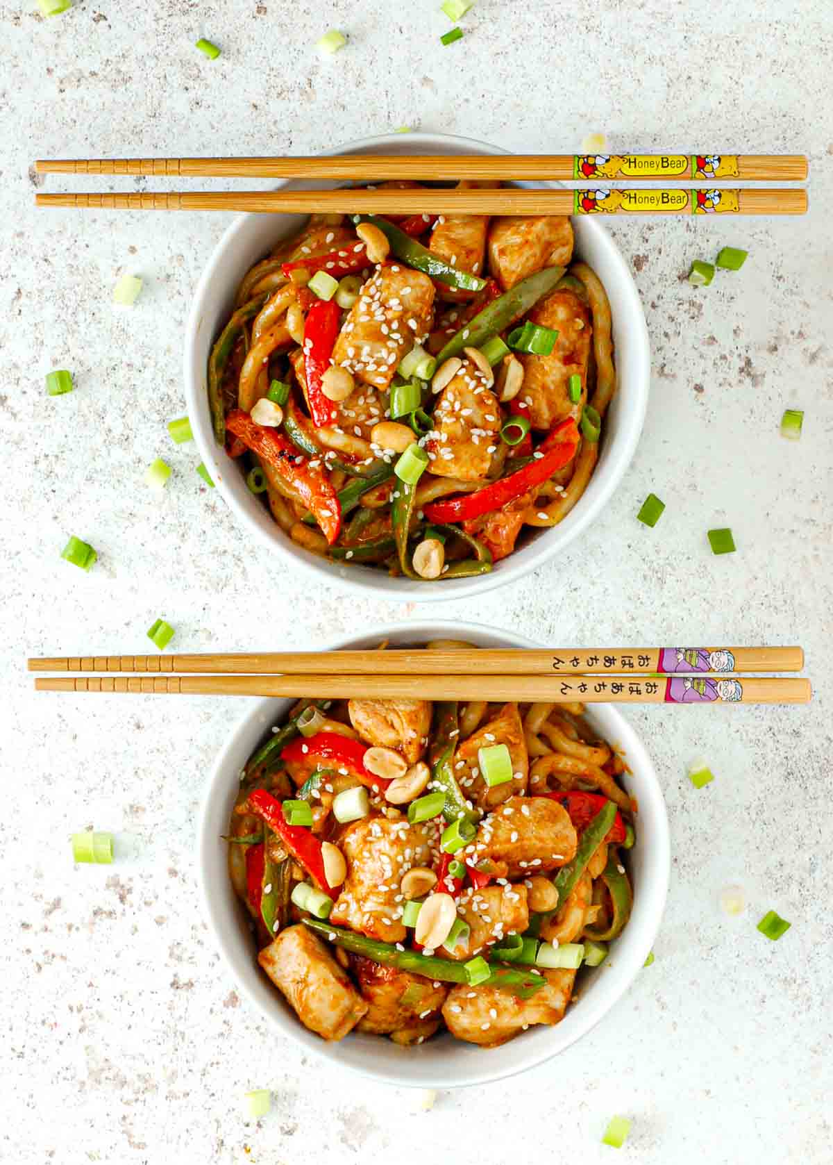 Two bowls of chicken stir fry on a white background with chopsticks