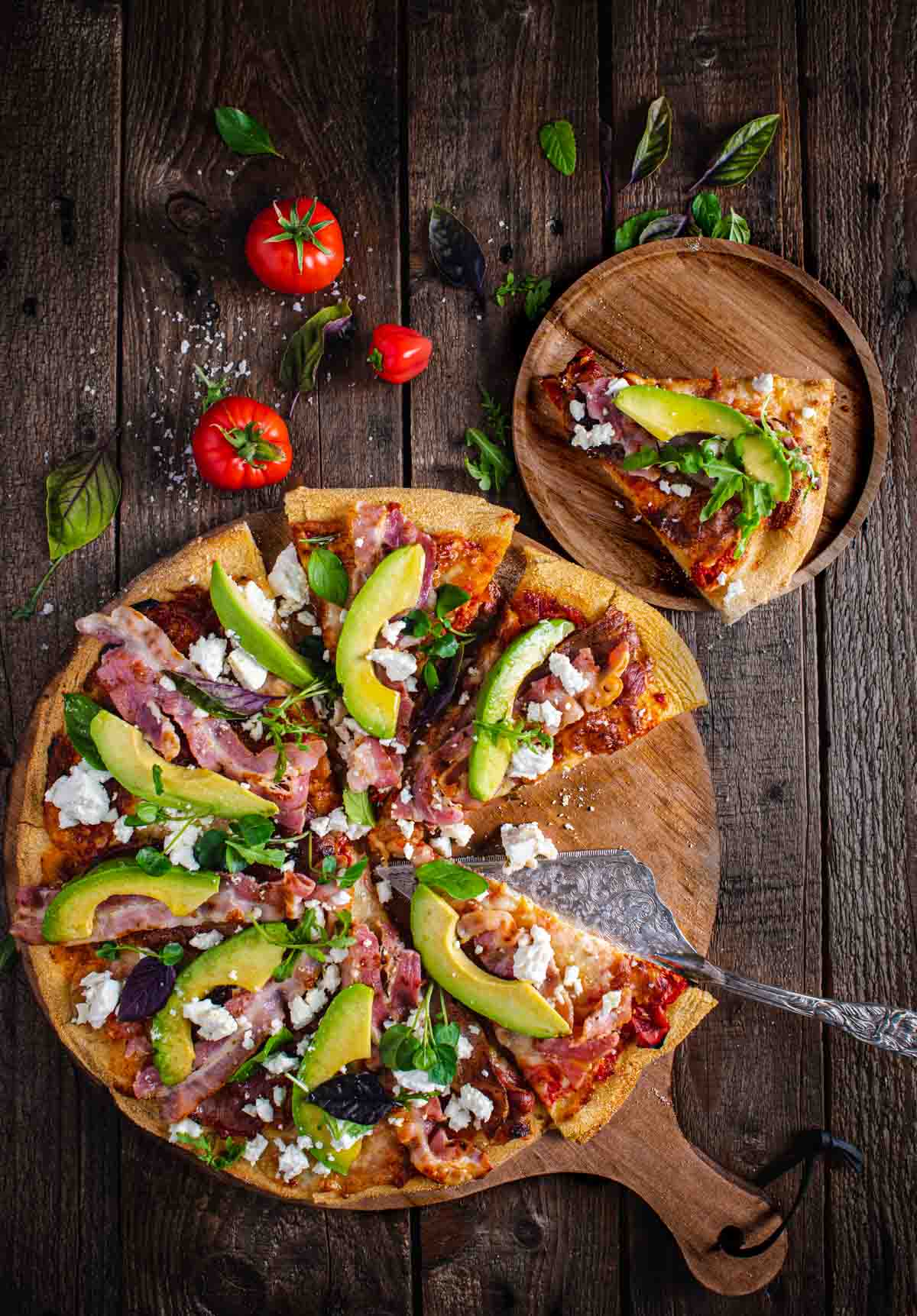 A large pizza on a wooden board, one slice of pizza to the side on a wooden plate