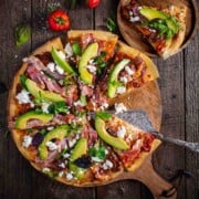 A large pizza on a wooden board, one slice of pizza to the side on a wooden plate