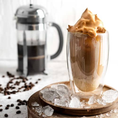 Iced coffee with condensed milk in a tall glass on a wooden plate