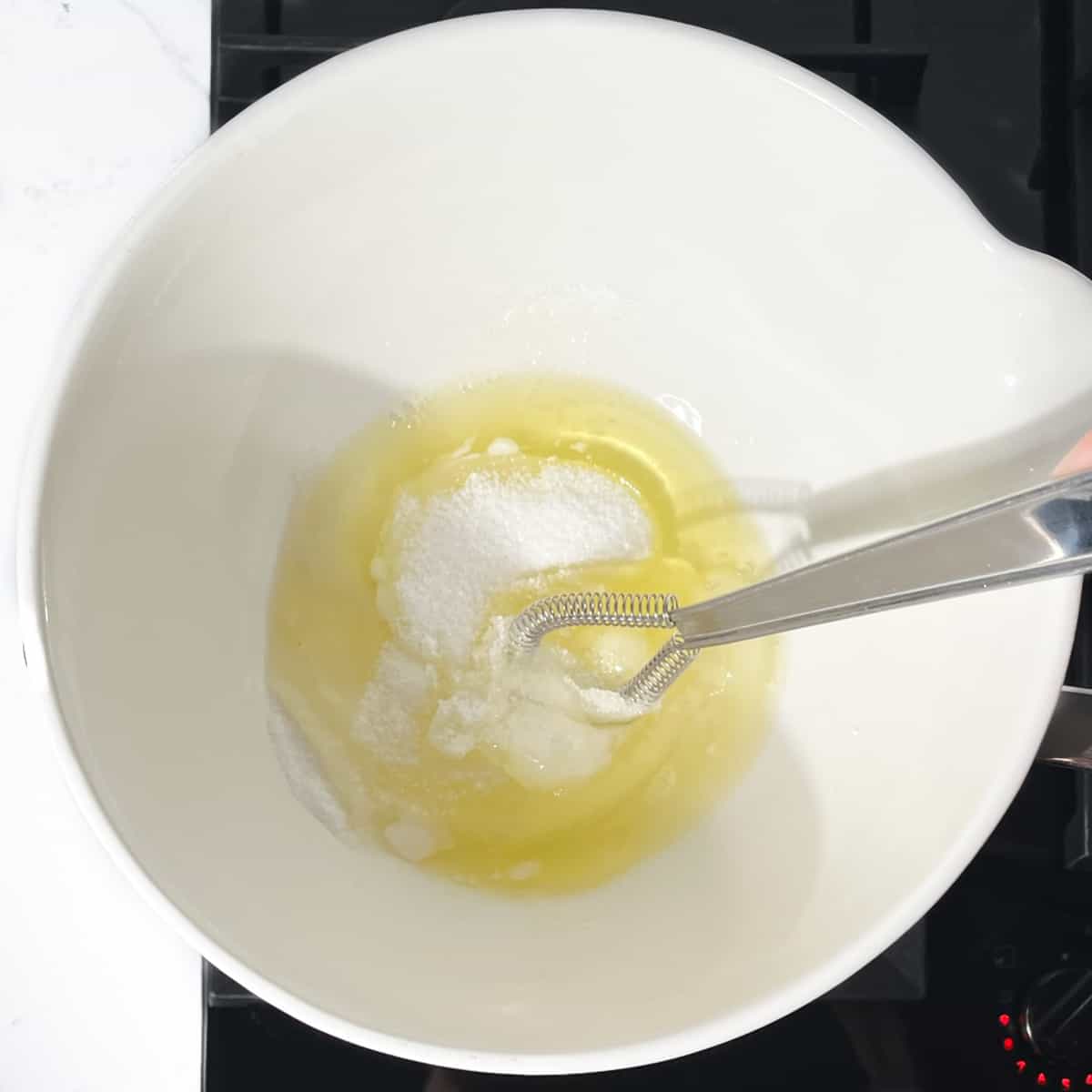 A bowl with egg whites and sugar on top of a saucepan with boiling water on the stovetop.