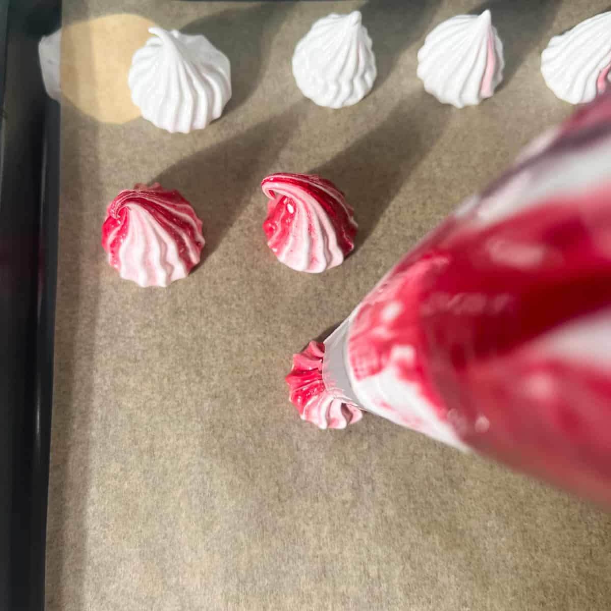Piping mini meringues onto a baking sheet with a piping bag.
