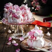 One mini rose pavlova served on a plate with three more pavlovas served in a glass cake stand