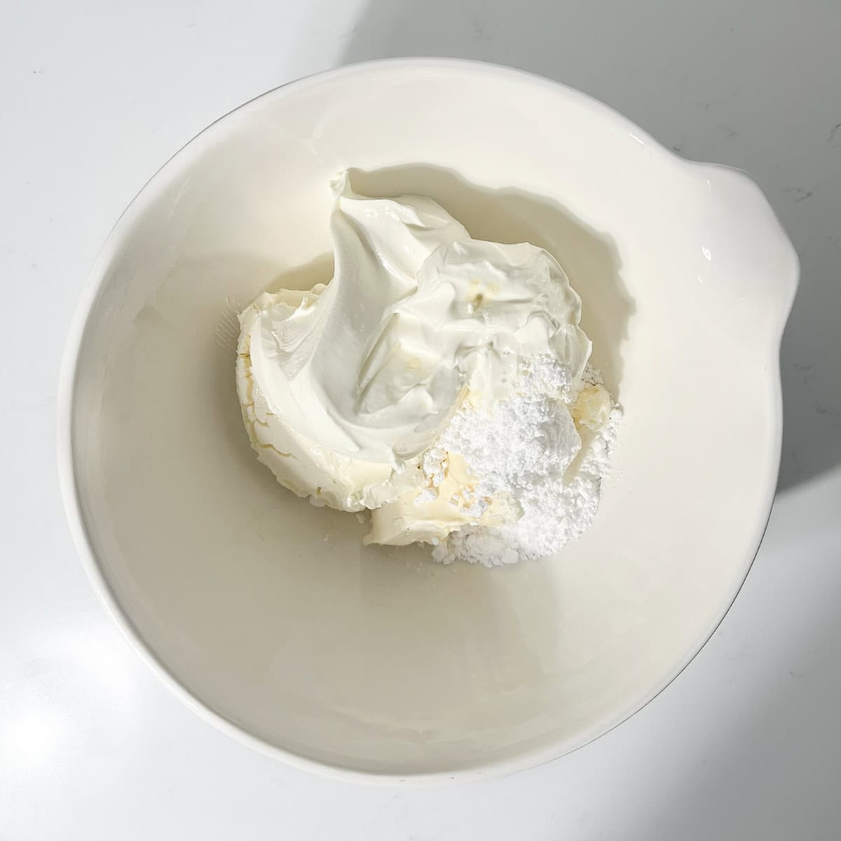 Adding icing sugar, mascarpone and cream cheese to a large white bowl.