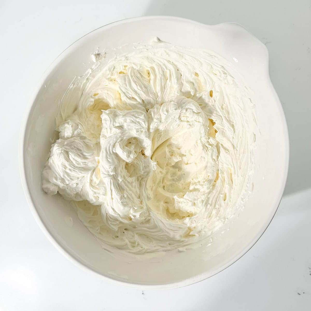 Cream cheese and mascarpone whipped in a large white bowl.