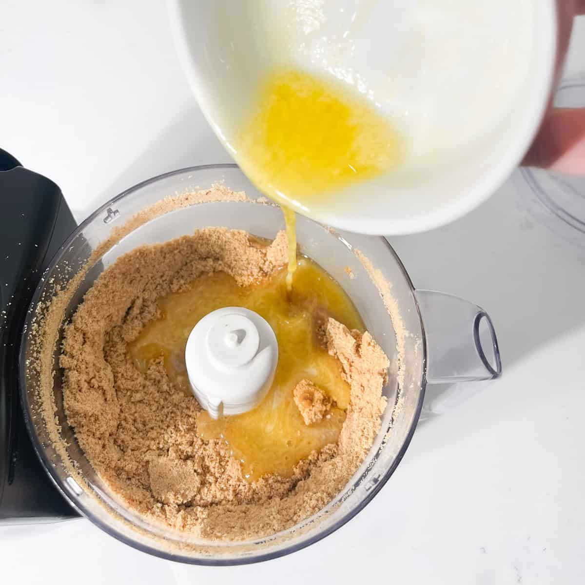 Adding butter to crushed cookie crumbs for the cheesecake crust.