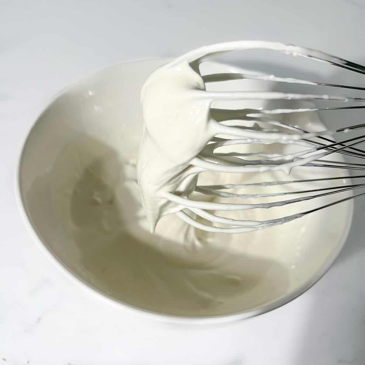 Showing cream at a soft peak on the beaters of an electric hand mixer.