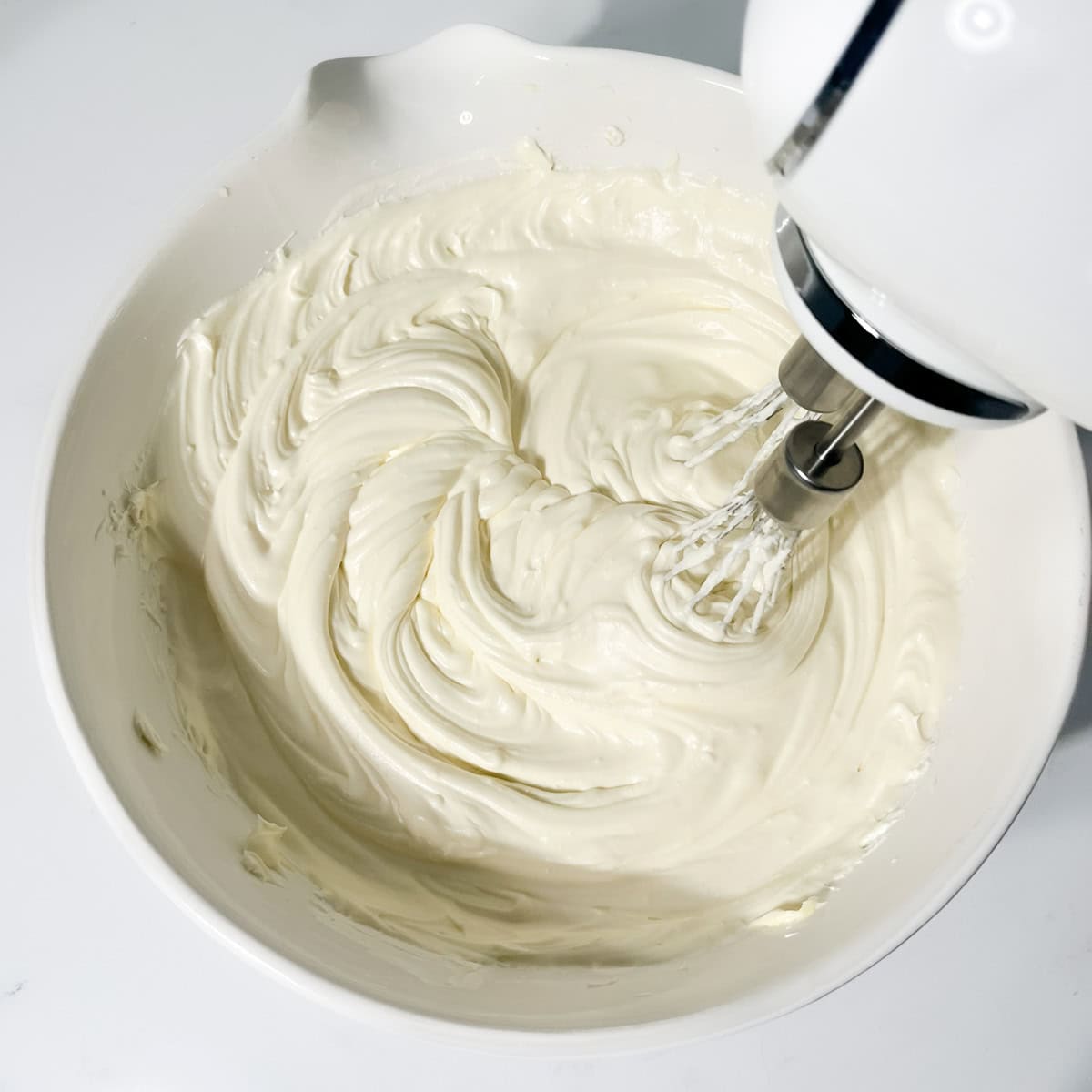 Whipping the cream for the no bake white chocolate and strawberry cheesecake in a large white bowl.