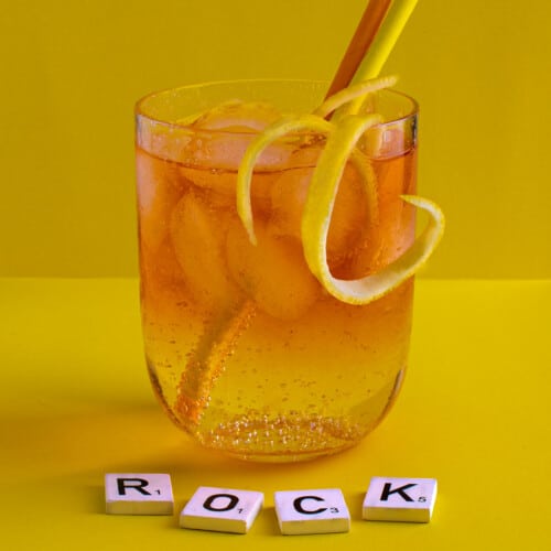 A medium glass of Rock shandy on a yellow background with an orange and yellow straw.