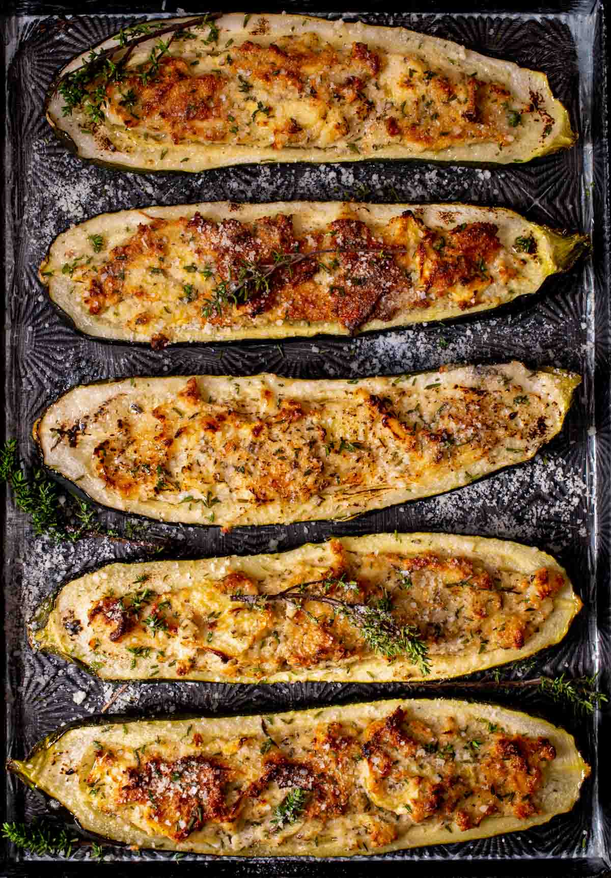 Stuffed courgettes on a baking sheet, sprinkled with thyme.