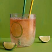 A glass of lemon, lime and bitters with two straws, on a green background.