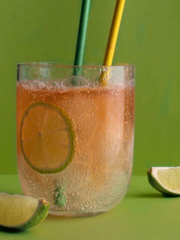 A glass of lemon, lime and bitters with two straws, on a green background.