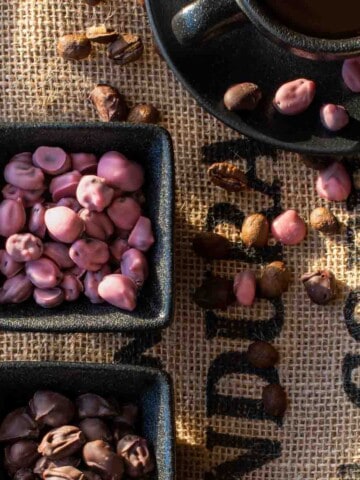 Ruby and dark chocolate covered coffee beans in black pots, on a coffee sack background.