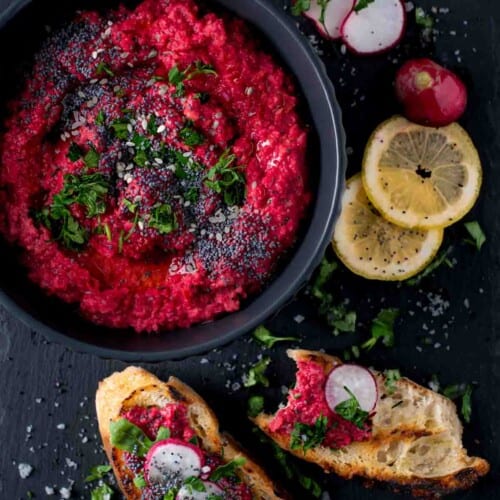 Beetroot hummus in a black bowl with toasted bread and lemon slices on the side.