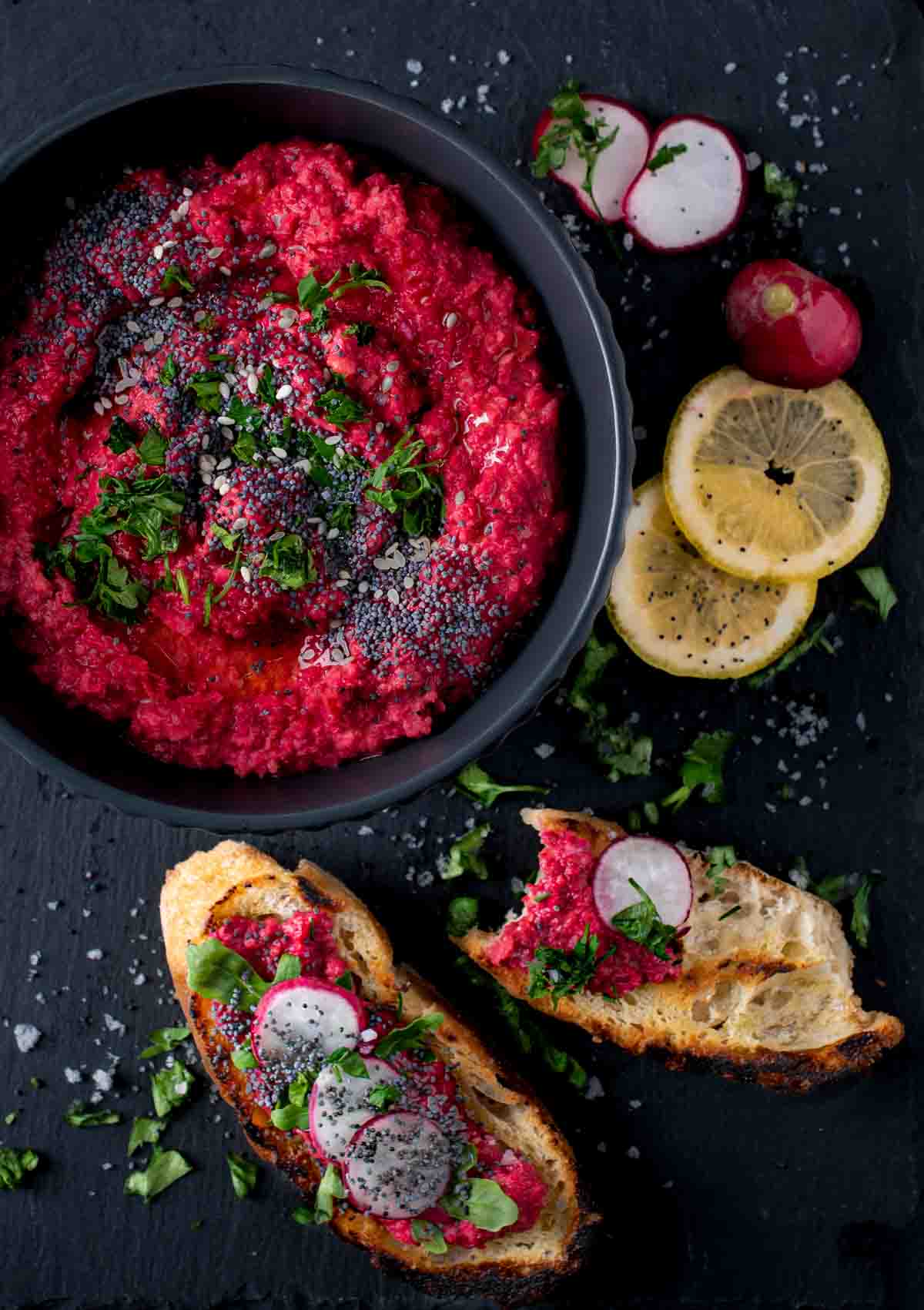 Beetroot hummus in a black bowl with toasted bread and lemon slices on the side.