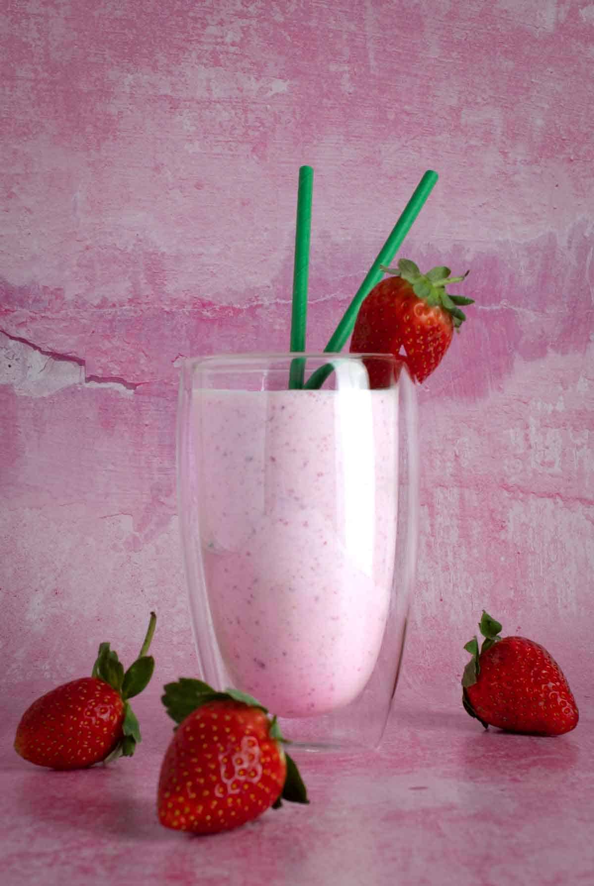 Strawberry lassi in a tall glass with four strawberries in the foreground.