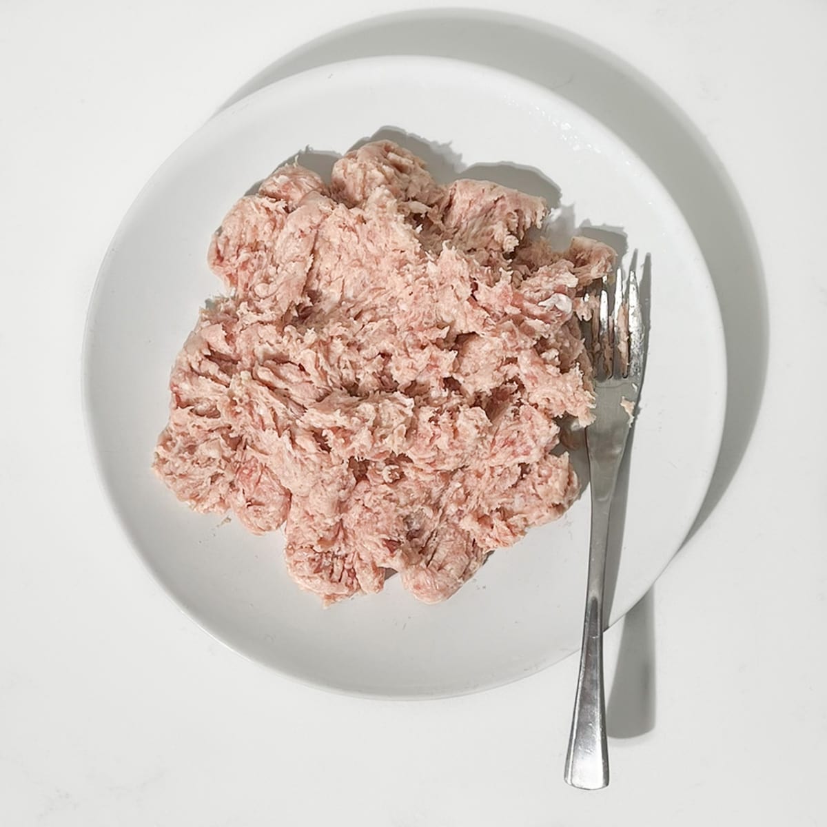 Breaking up the sausage meat with a fork on a white plate.