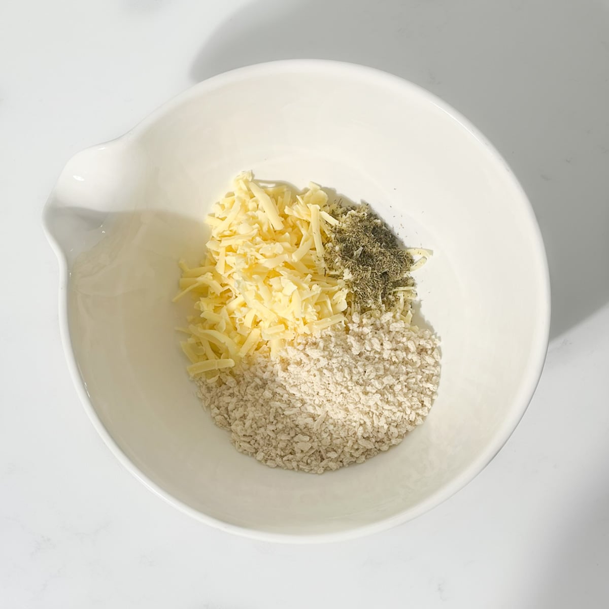 Breadcrumbs, cheese and herbs in a large white bowl.