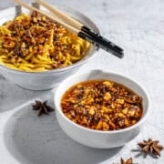 A bowl of crispy chilli oil alongside a bowl of egg noodles.