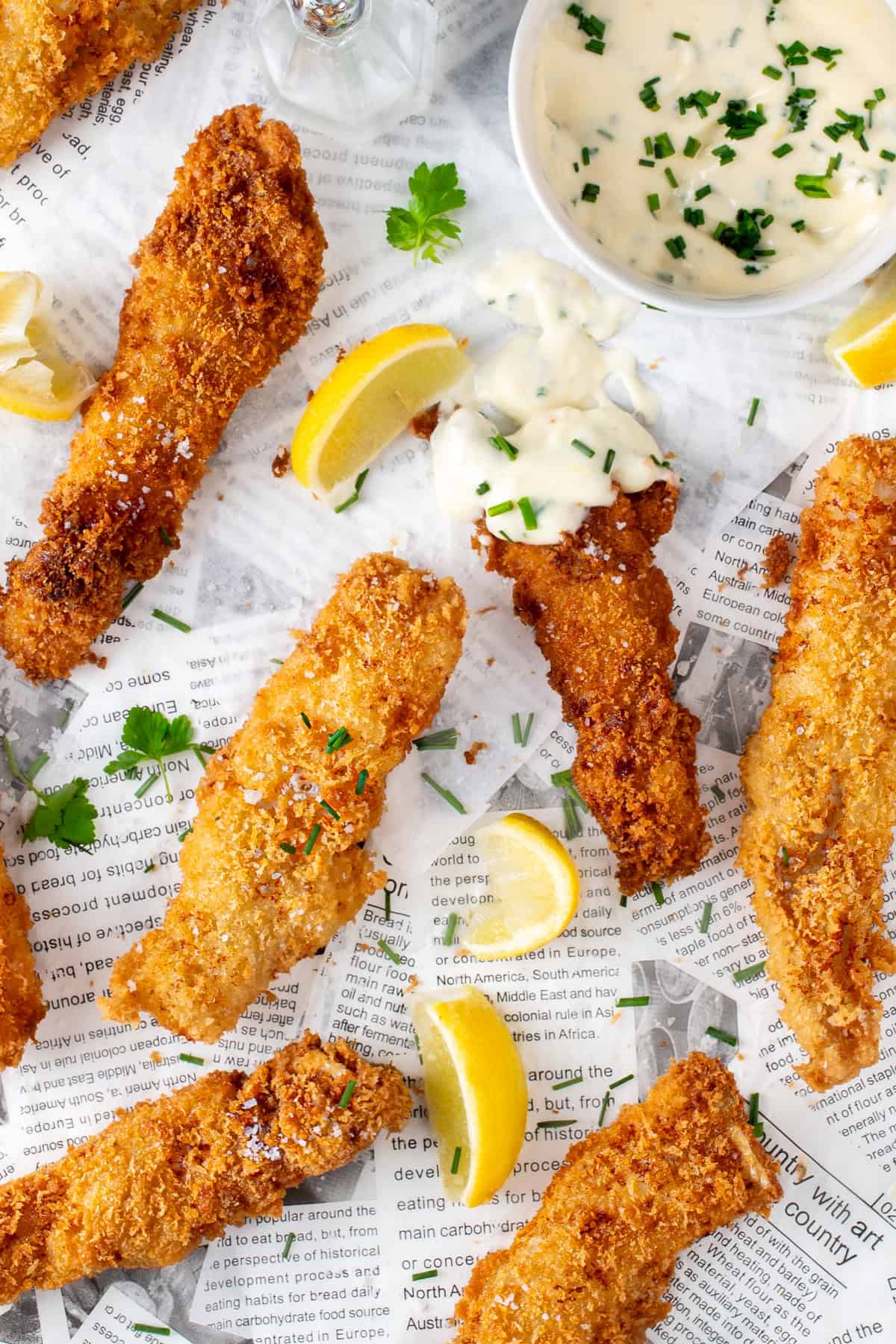 Crispy fish goujons with lemon wedges and garlic mayo on newspaper-style paper.