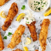 Crispy fish goujons with lemon wedges and garlic mayo on newspaper-style paper.