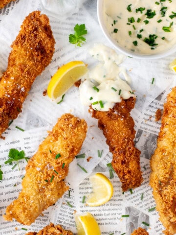 Crispy fish goujons with lemon wedges and garlic mayo on newspaper-style paper.
