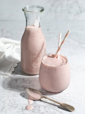 A glass and a carafe of strawberry lassi on a white background.