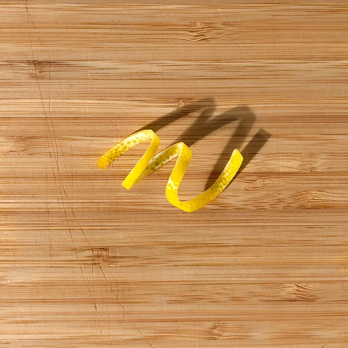 A lemon peel twisty on a wooden chopping board.