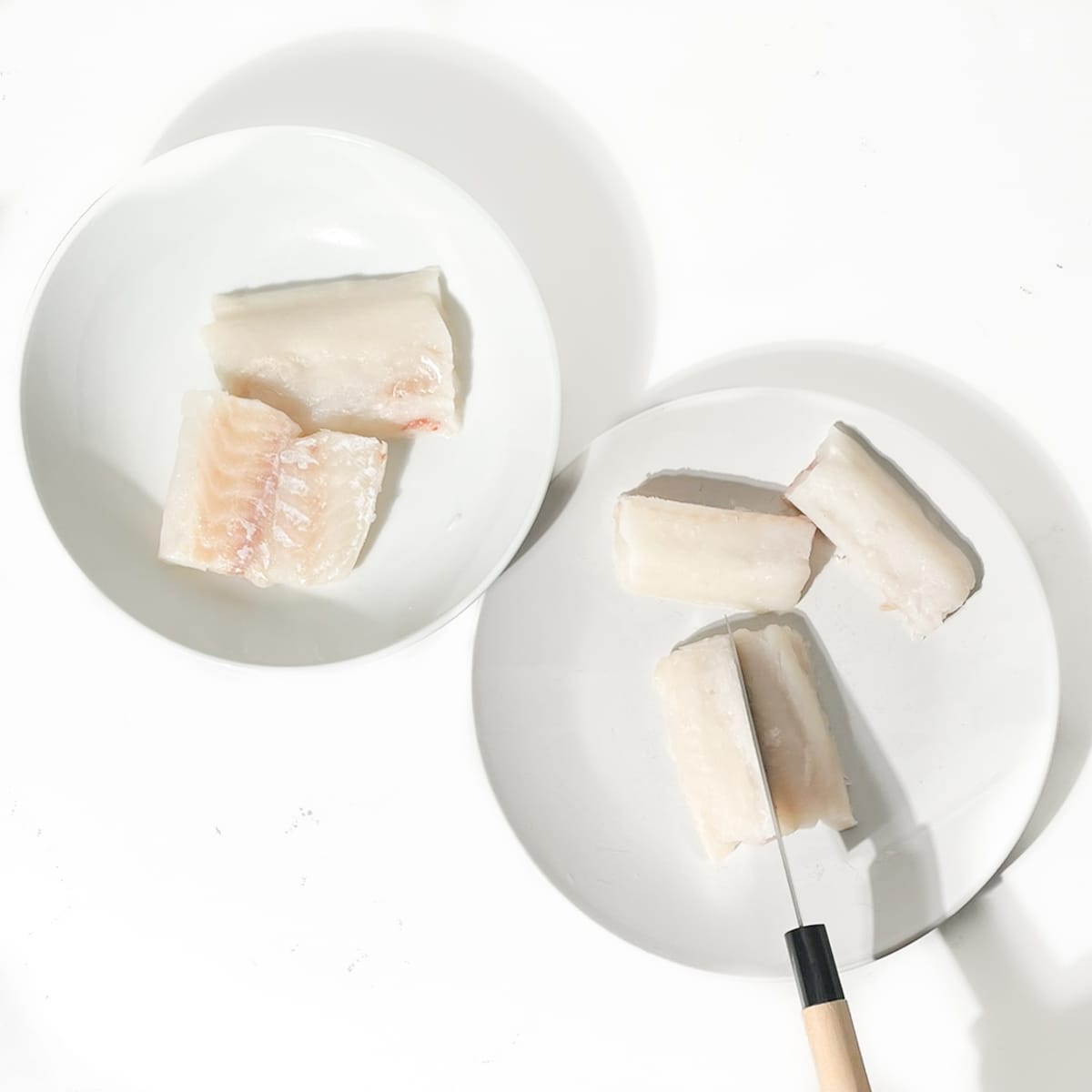 Cutting the fish fillets lengthways on a white plate.