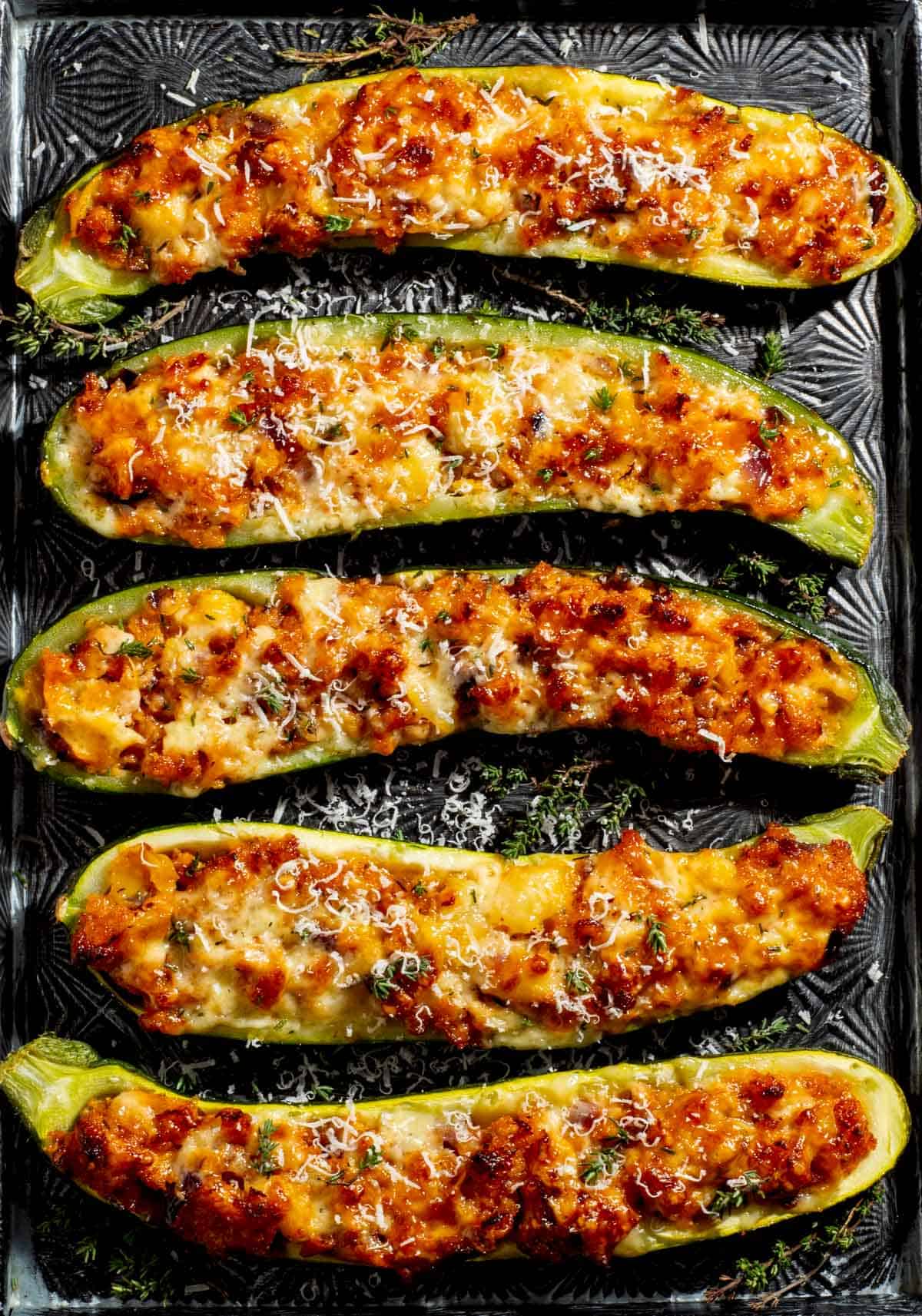 Stuffed courgettes on a baking tray with parmesan grated over.