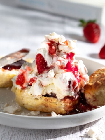 One halved scone topped with Eton mess topping and a plate of scones in the background.