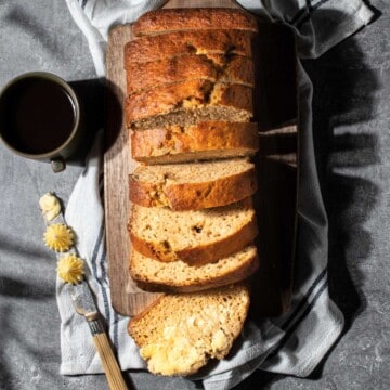 A loaf of 4-ingredient banana bread sliced into 9 slices. One slice is buttered.