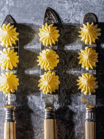 Three knifes with three butter rosettes on each blade.
