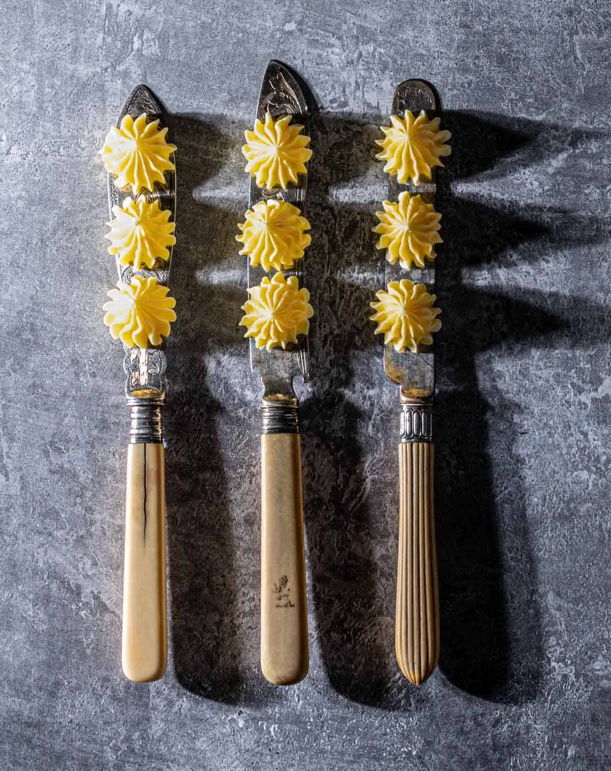Three knifes with three butter rosettes on each blade.