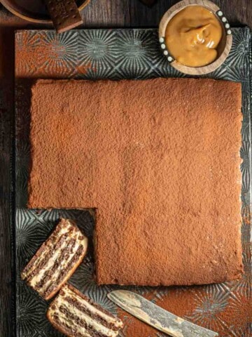 Chocotorta on a metal tray with one slice cut out. The slice is laying on it's side to show the layers of the dessert.