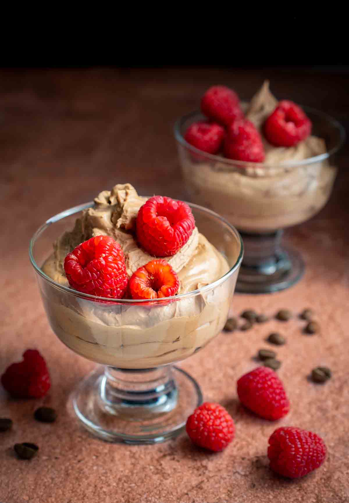 Two bowls of coffee mousse with raspberries on top.