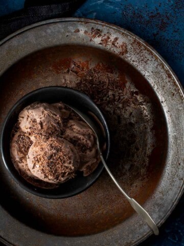 A bowl containing a few scoops of dark chocolate ice cream, on a metal plate.