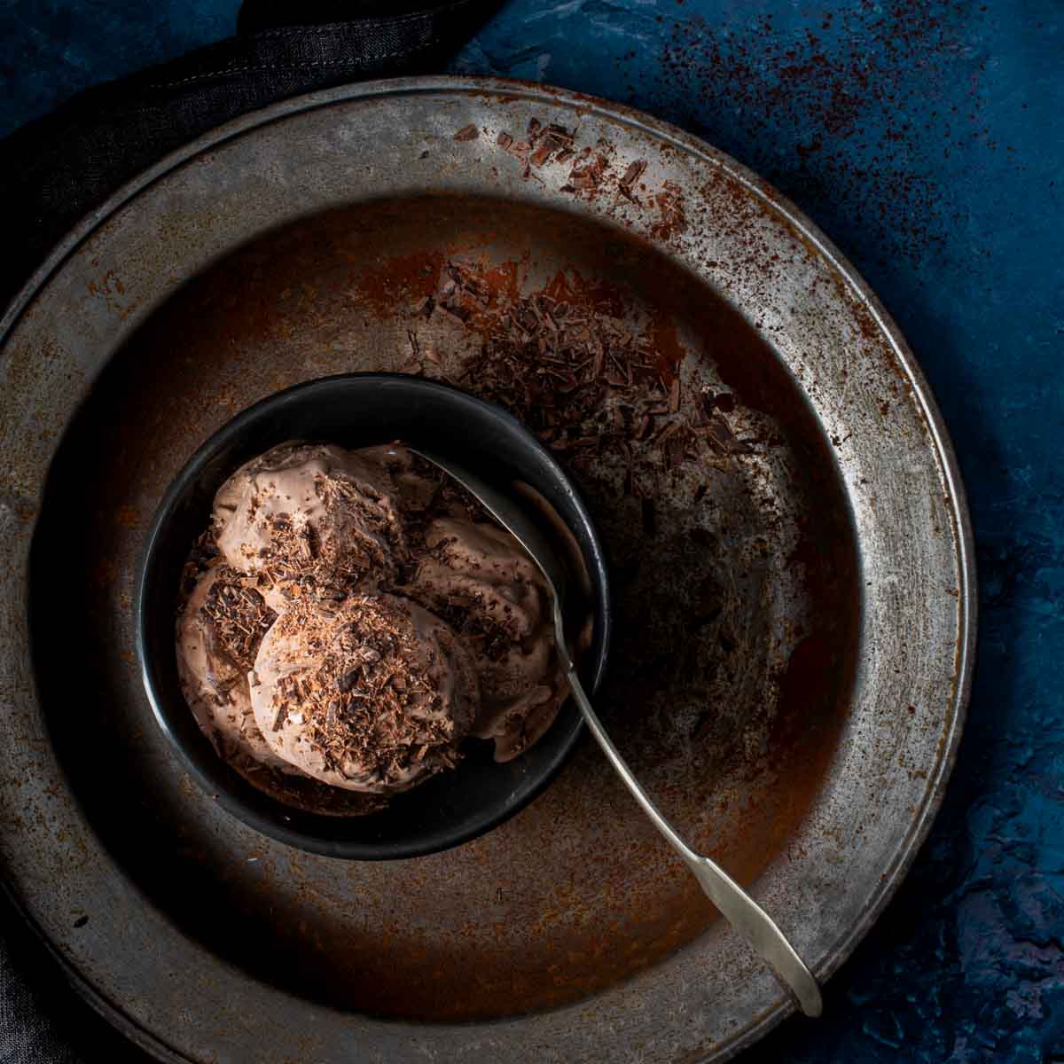 A bowl containing a few scoops of dark chocolate ice cream, on a metal plate.