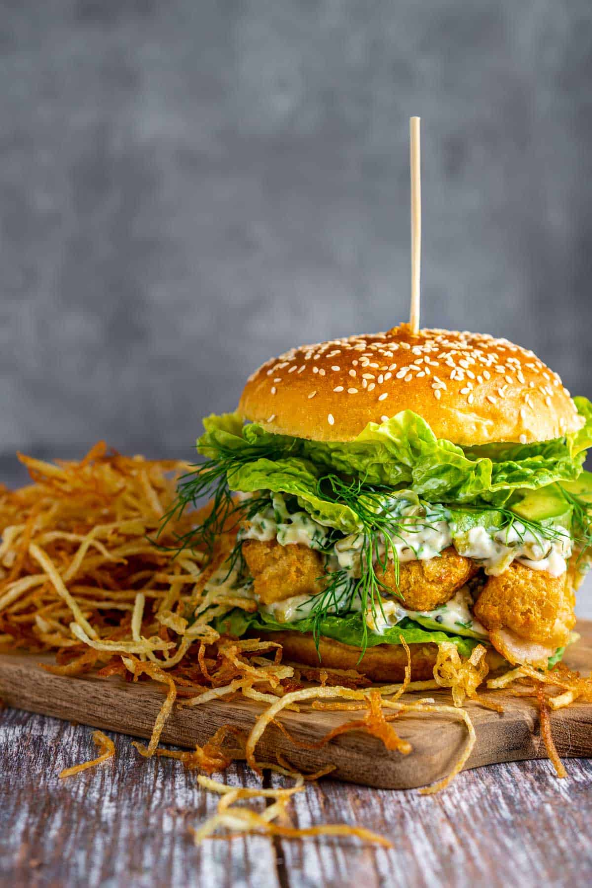 An ultimate fish finger sandwich on a wooden board with a side of shoestring fries.