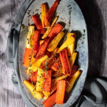 Honey roasted carrots and parsnips on a grey serving tray.