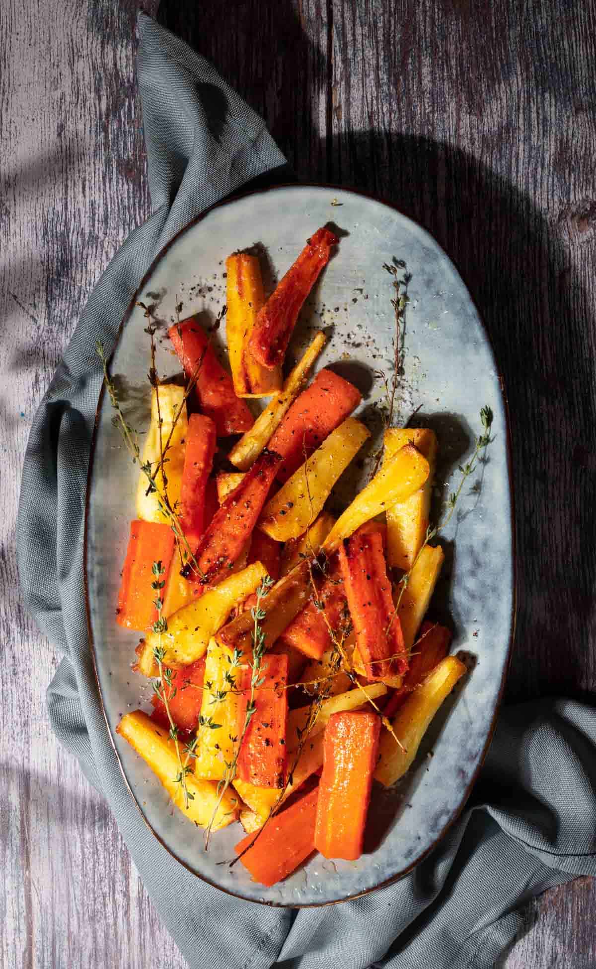 Honey roasted carrots and parsnips on a grey serving tray.