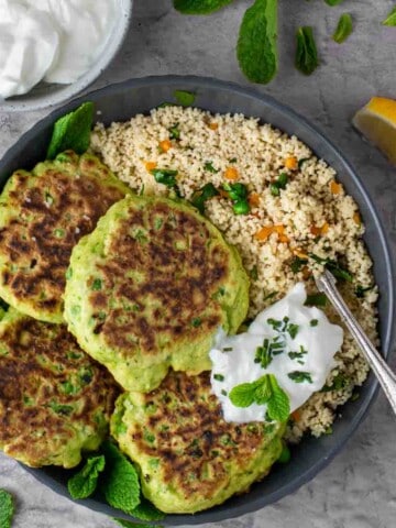 Four pea fritters in a bowl with a portion of couscous. and a dollop of greek yoghurt.