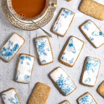 Spice biscuits, or soetkoekies, scattered across a white table with a cup of tea on the side.