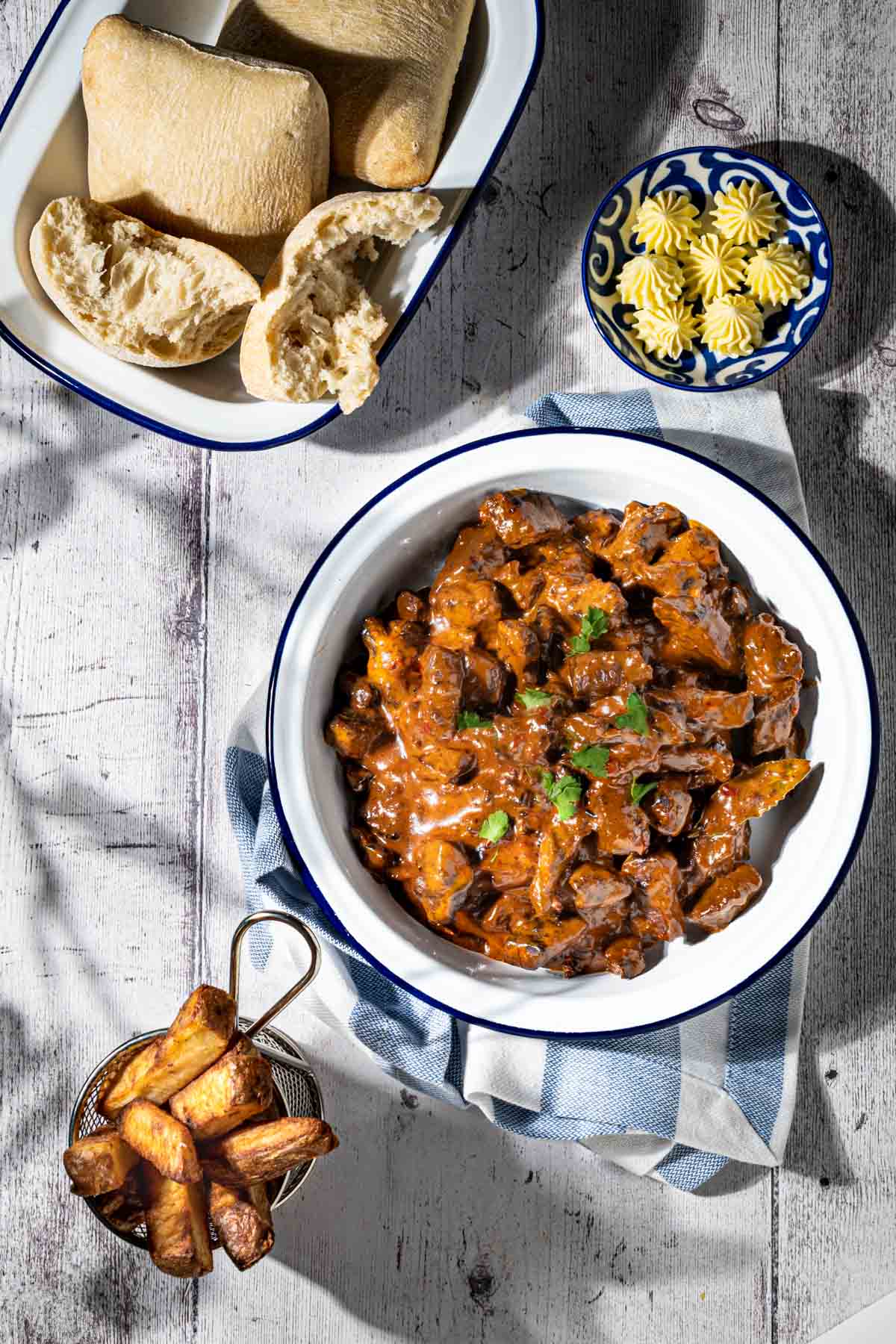 Trinchado in a white bowl with a dish of bread rolls and a small basket of chips.