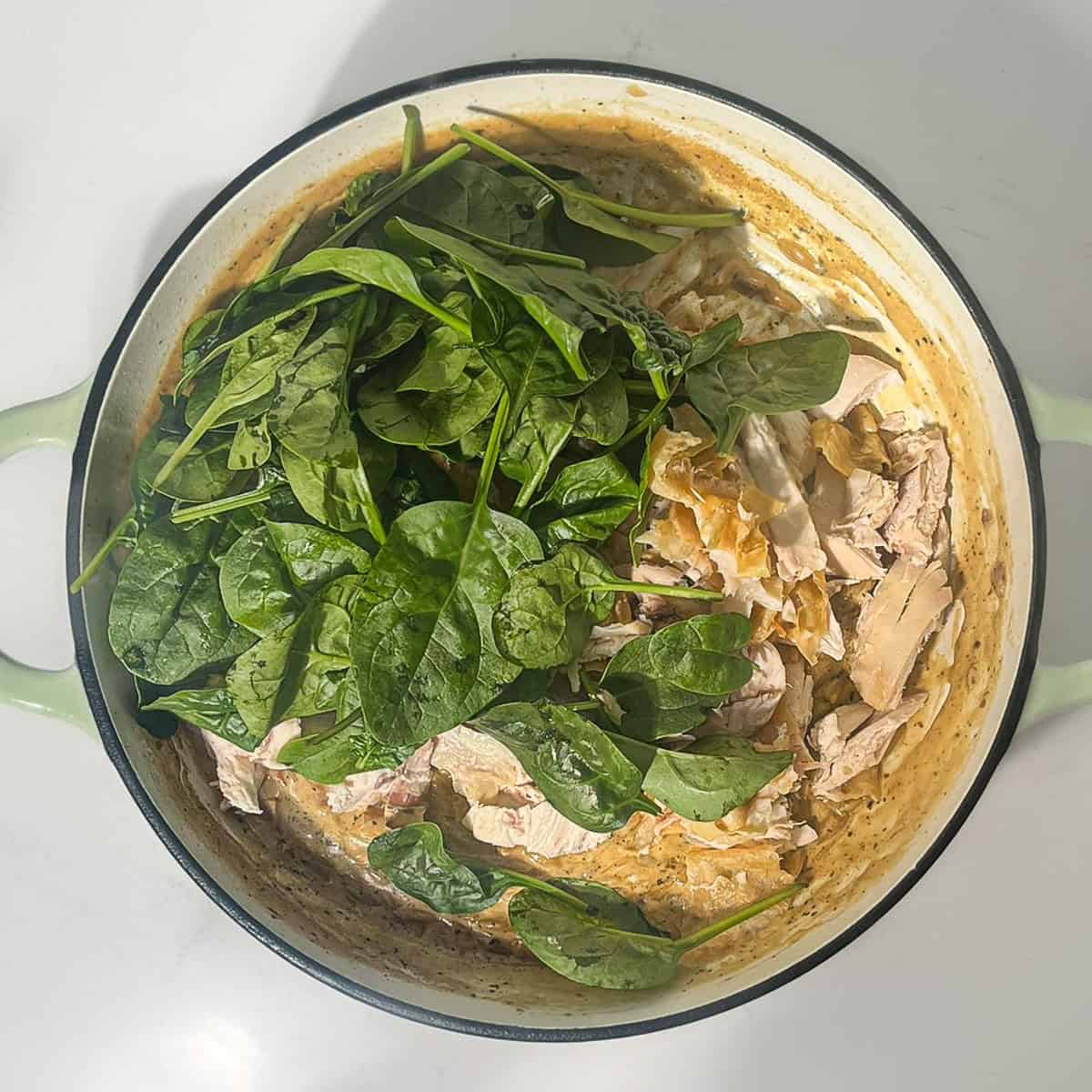 Adding spinach and parmesan to the lemon chicken orzo pasta in a large saucepan.