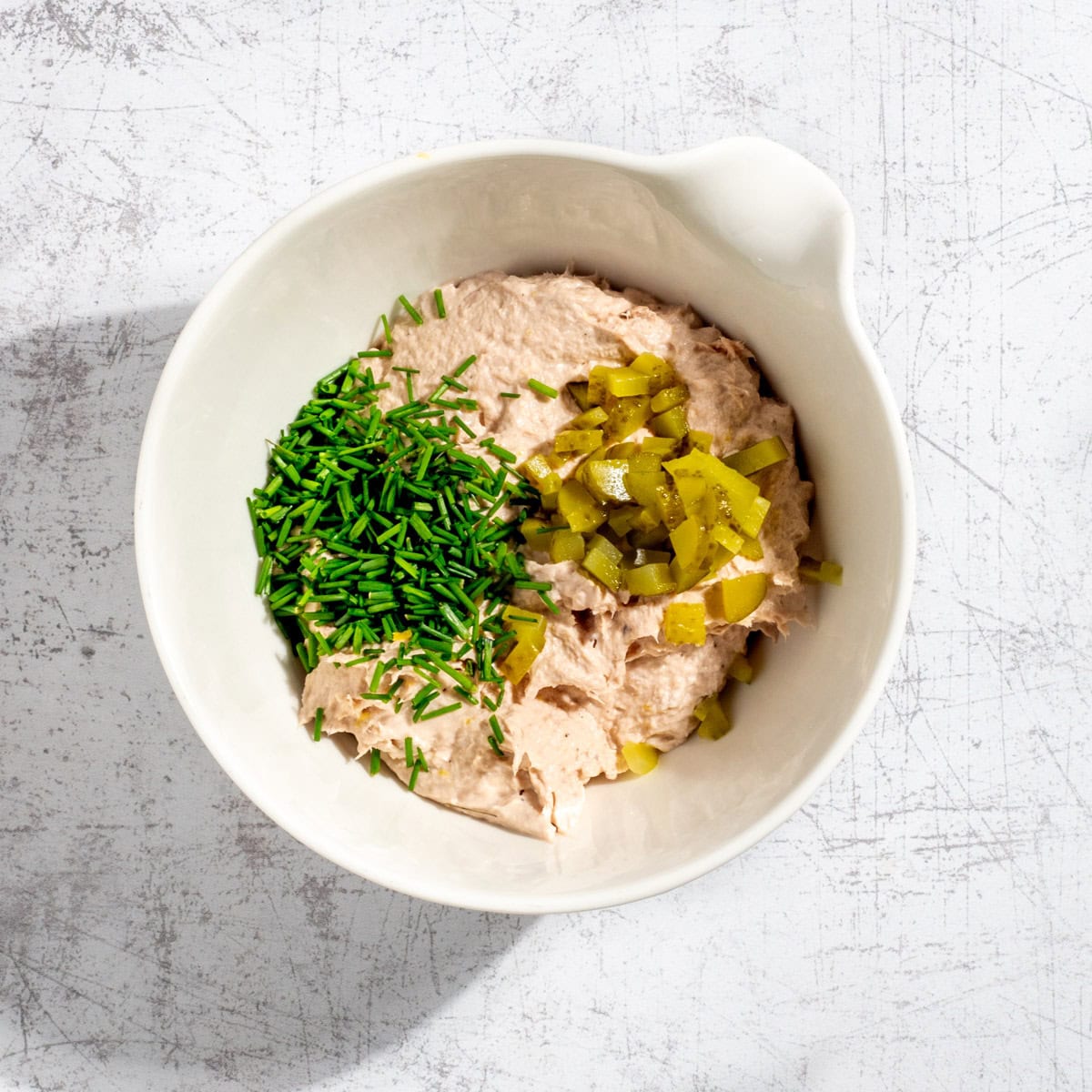 Blended tuna pate in a white bowl with chopped chives and gherkins.